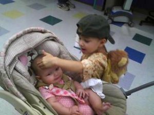 Jayden, backpack on, patting baby sister